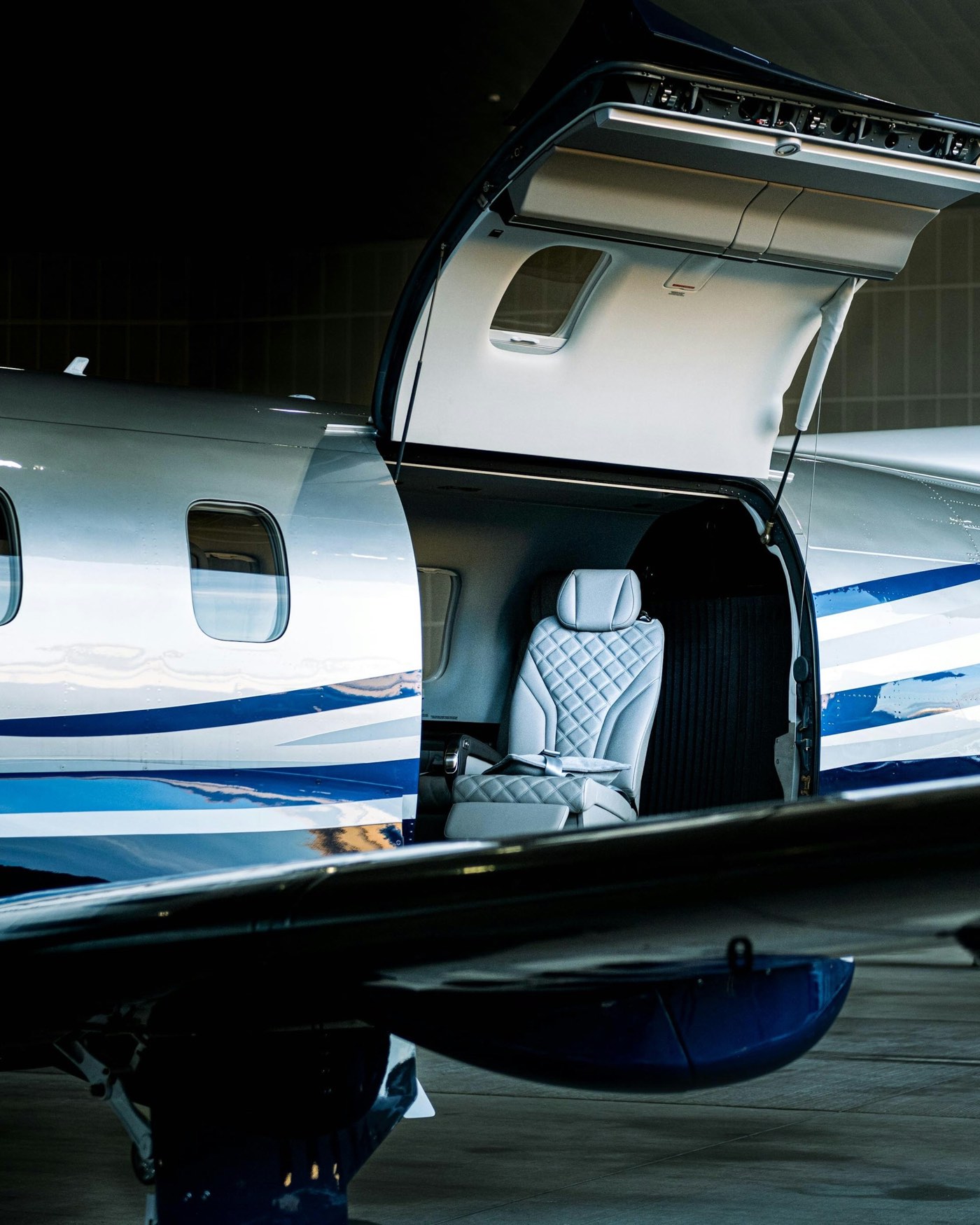 The open cabin door of a turboprop in a hangar, with a quilted leather seat inside.